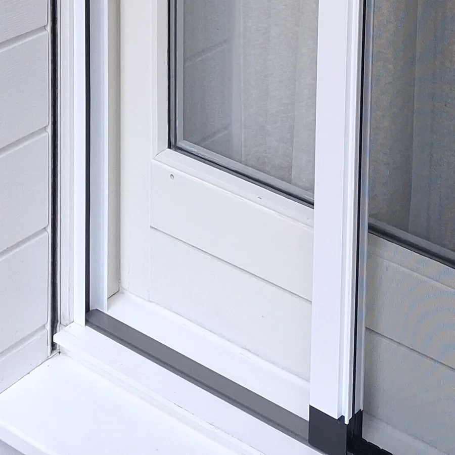 Angle bas d’une porte-fenêtre coulissante blanche de Vétraz-Monthoux : seuil, montant et extrémité de la barre de tirage de la moustiquaire.