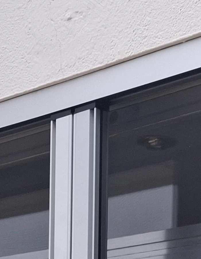 Haut d’une fenêtre de Vétraz-Monthoux : les deux profils verticaux des moustiquaires se rejoignent sous le linteau, toile tendue de chaque côté.