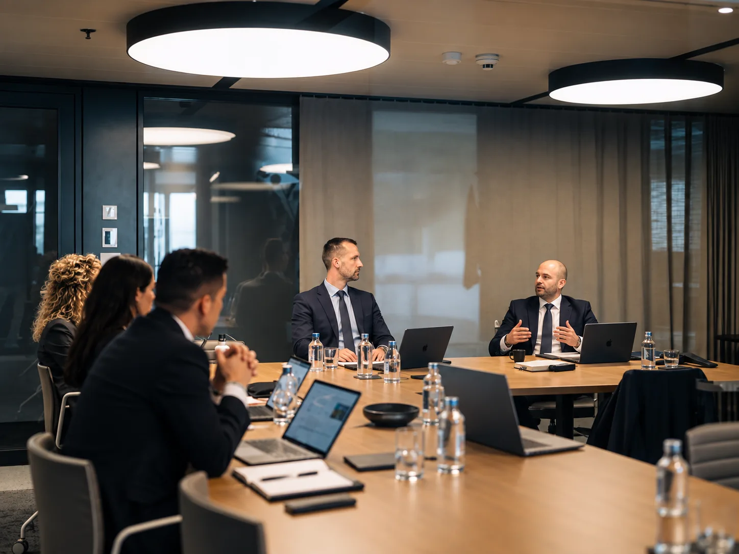 Colleagues in discussion around a long boardroom table with laptops