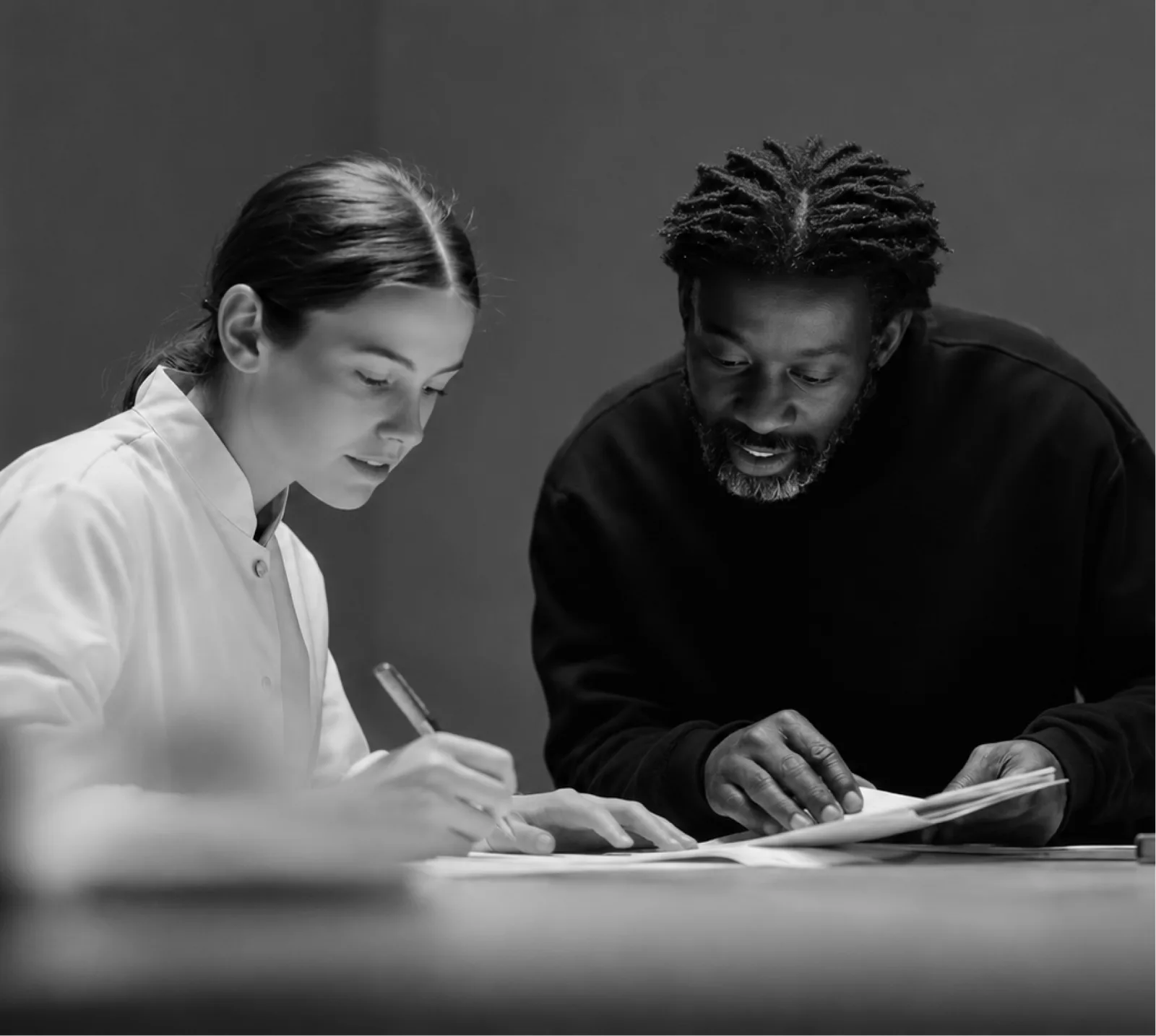 Two colleagues reviewing papers together at a table, in black and white
