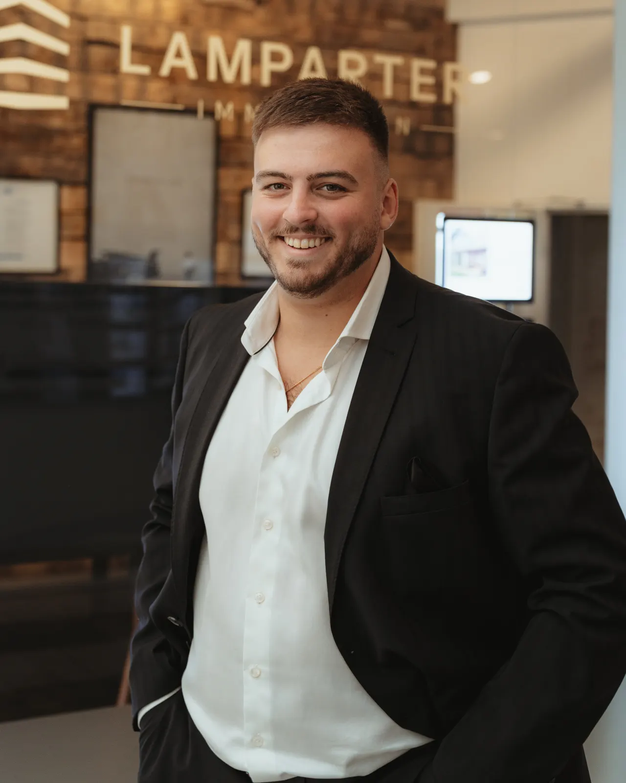 Kelwin Lamparter, Inhaber von LAMPARTER Immobilien, im Büro in Coesfeld vor der Logowand