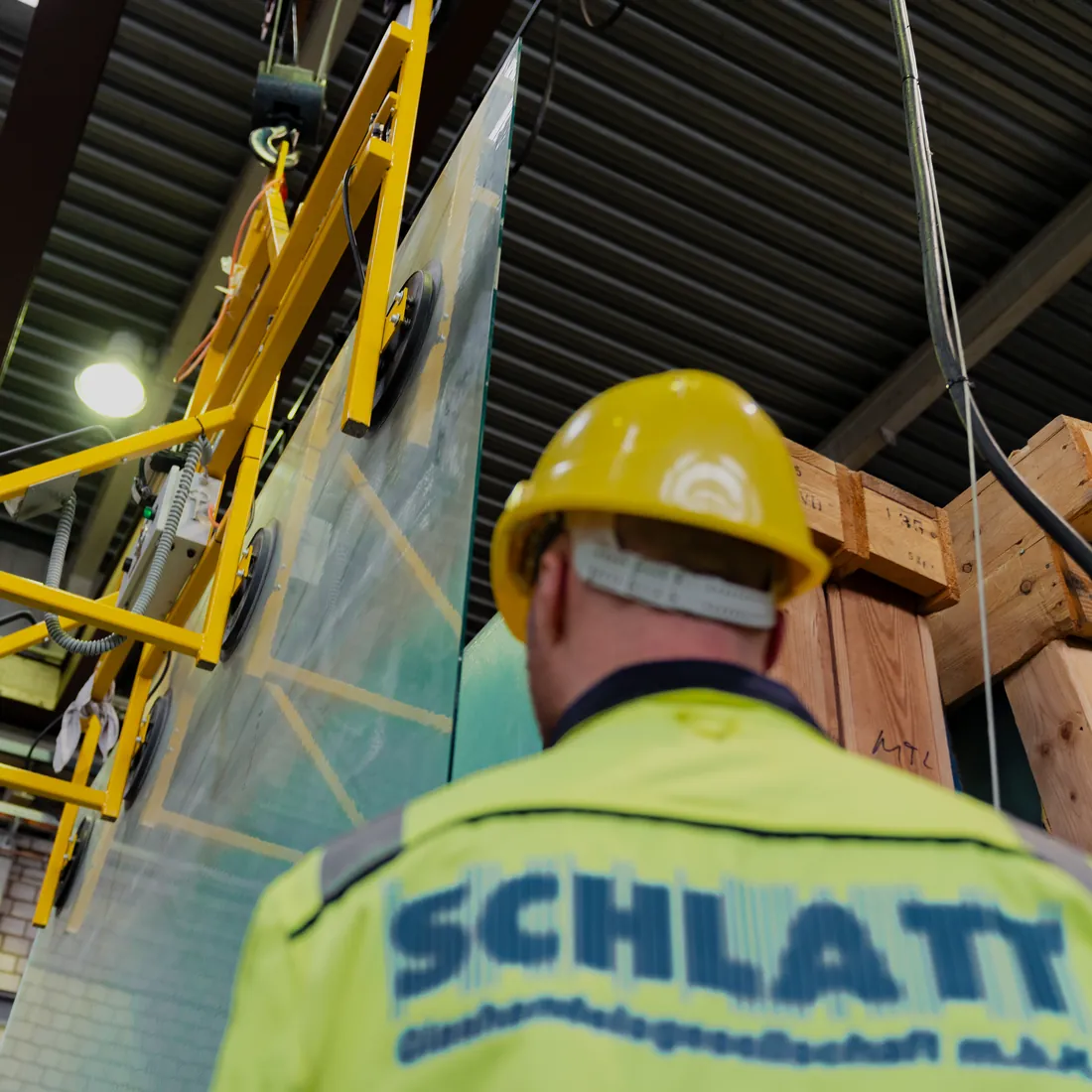 SCHLATT-Mitarbeiter mit Schutzhelm bewegt eine große Glasscheibe mit dem Vakuumheber