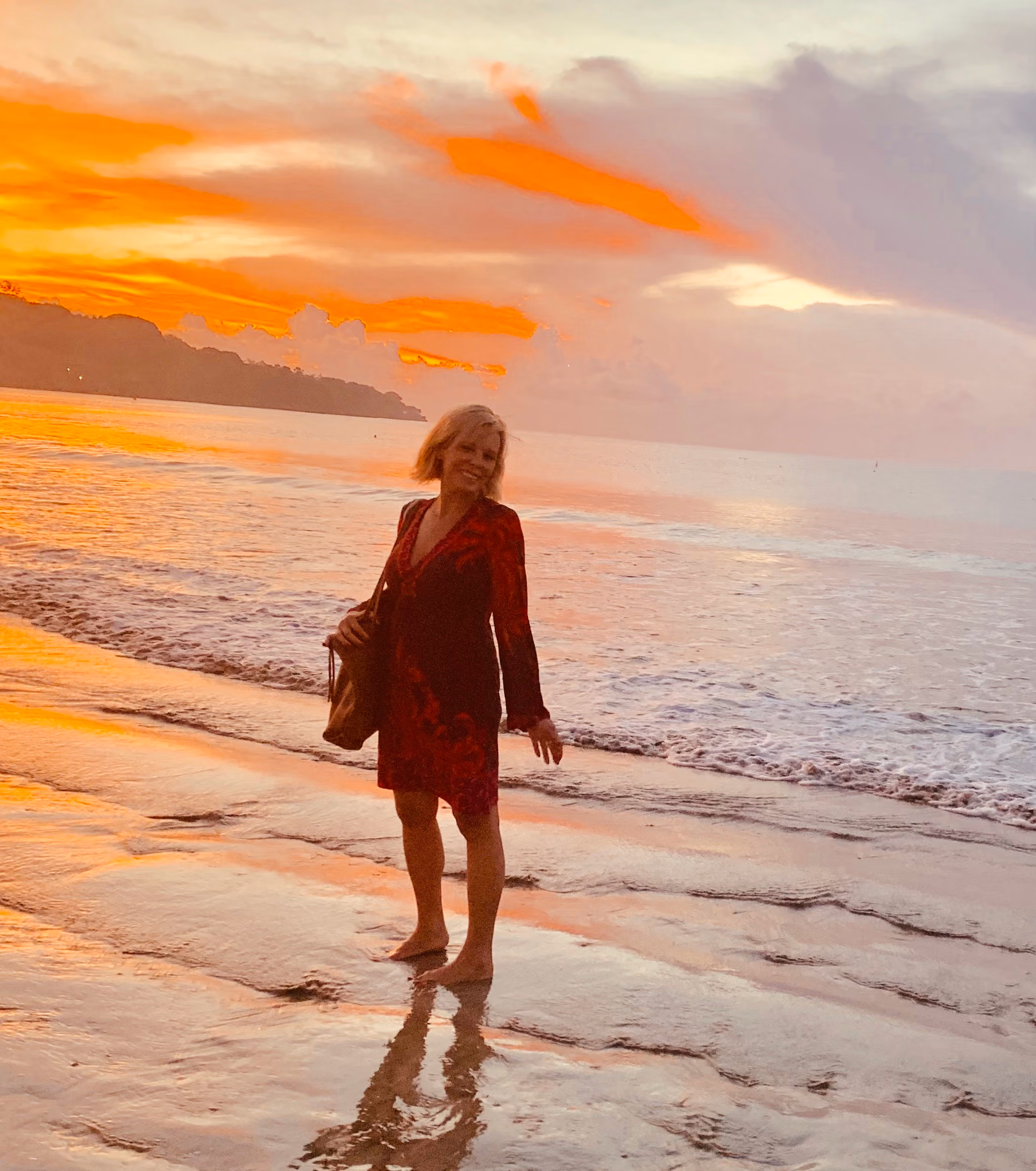 Dr. Lisa Leit standing barefoot on a beach beneath a vivid orange sunset.