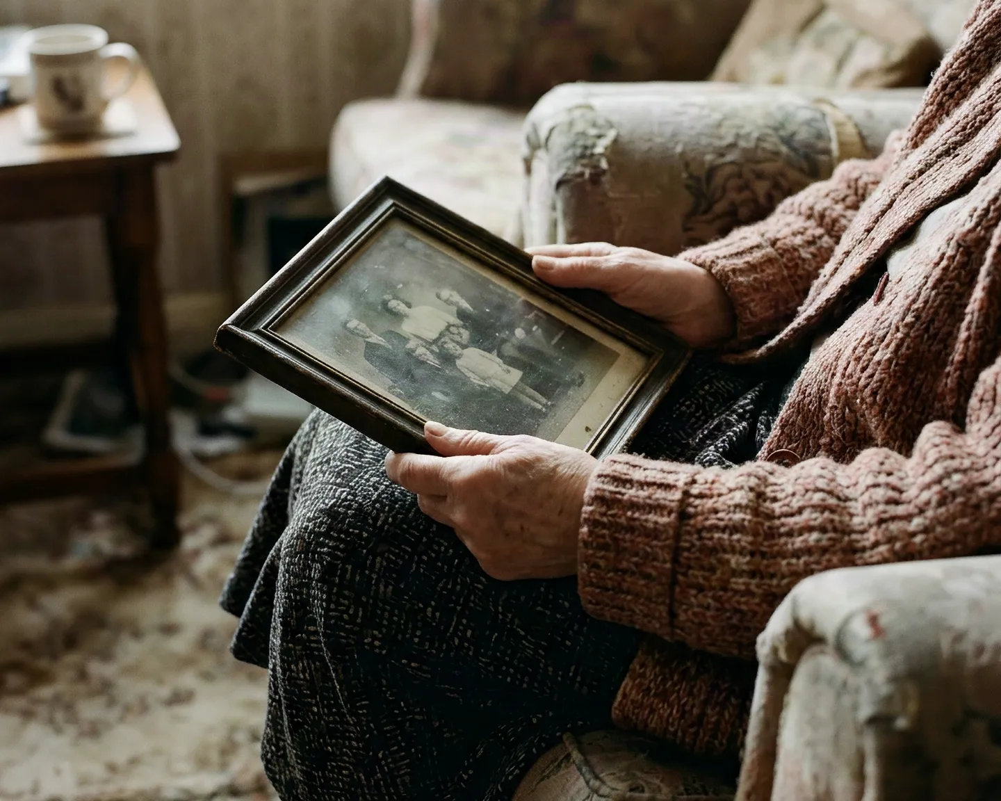 Hands holding an old family photograph in an armchair
