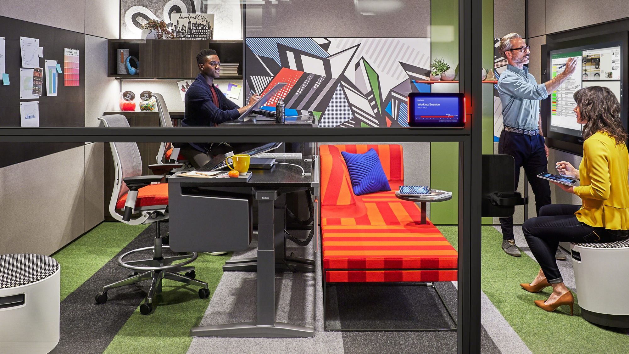 Steelcase workplace with people working at a height-adjustable desk and a digital whiteboard