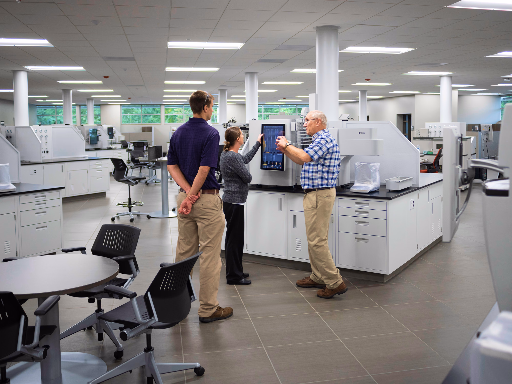 Three people reviewing the touchscreen interface of a LECO analytical instrument in a bright laboratory