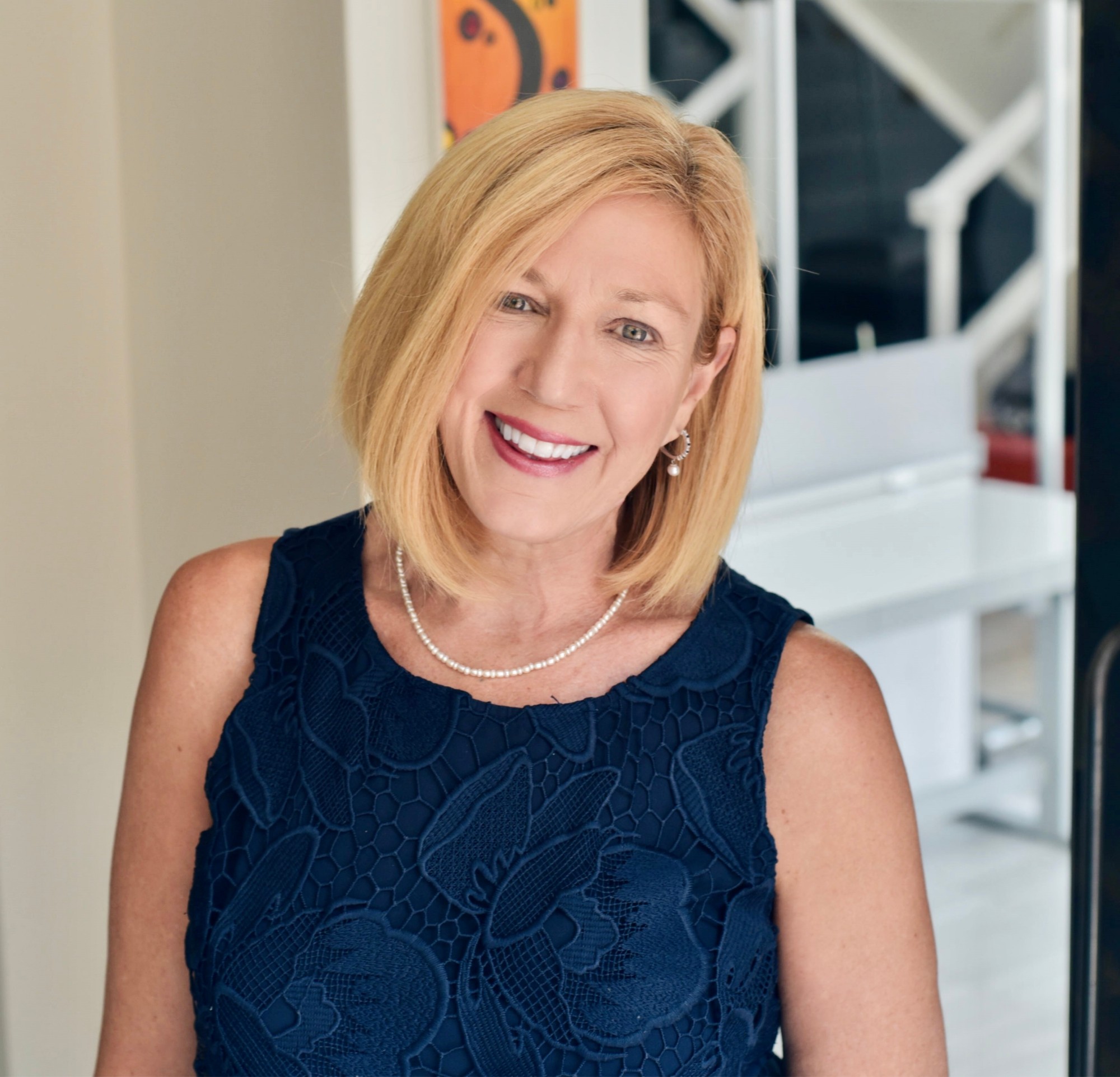 Kat Frati smiling, wearing a navy lace top and pearls.