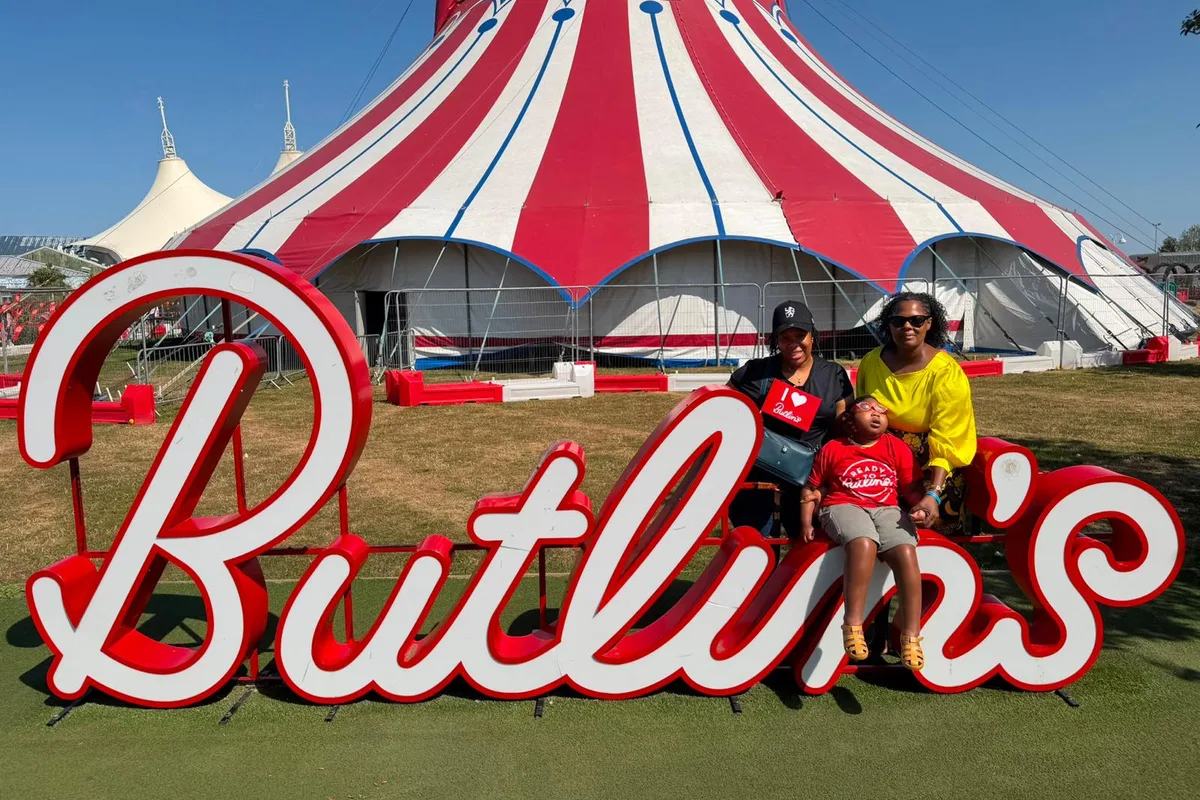 Two Oria carers with a young person on a day out at Butlin's, sitting on the Butlin's sign