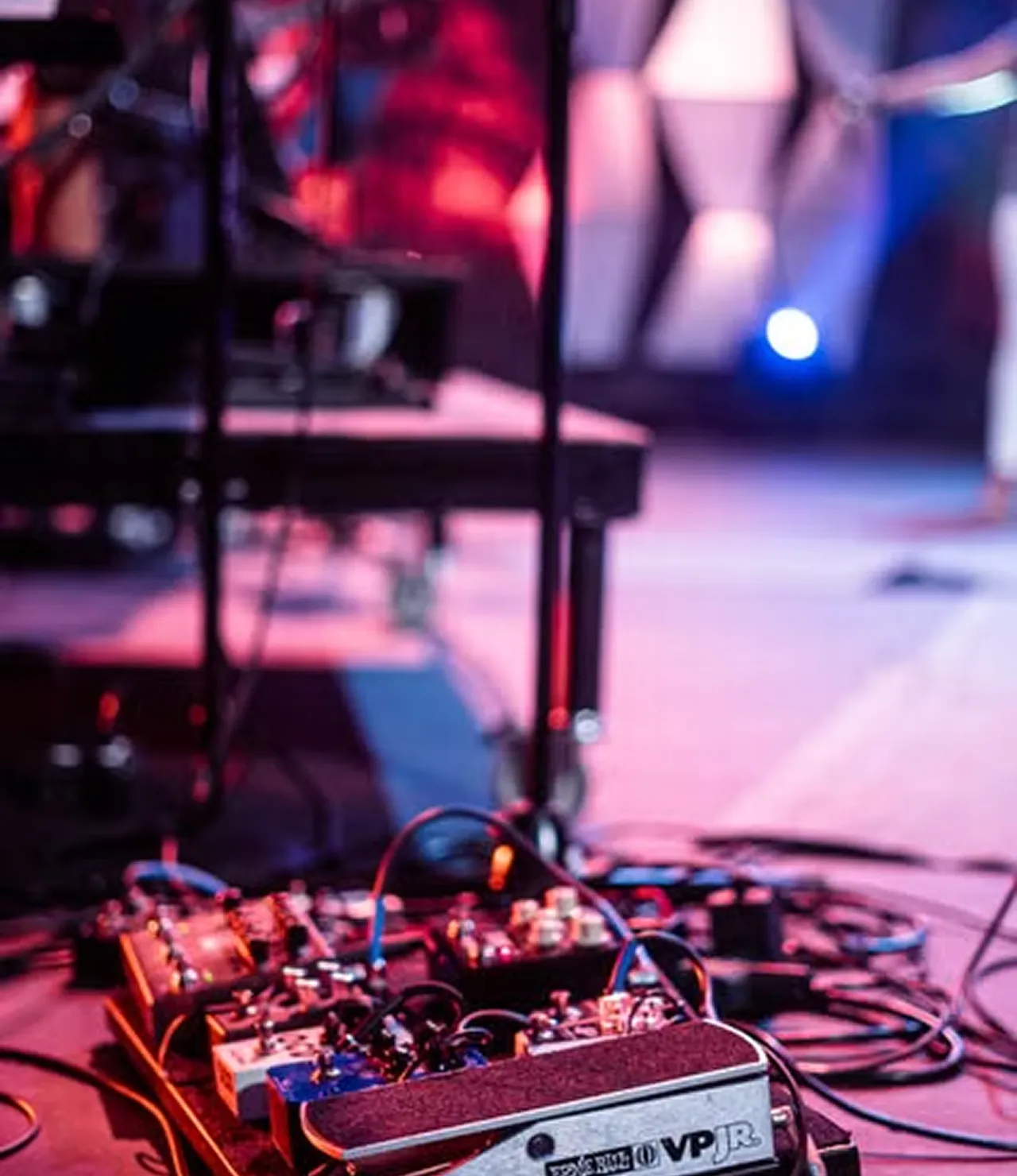 Guitar effects pedals wired up on a stage floor under purple and blue lights