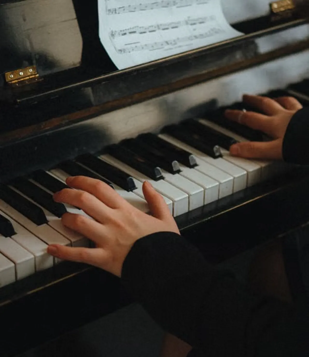 Hands playing an upright piano with sheet music on the stand