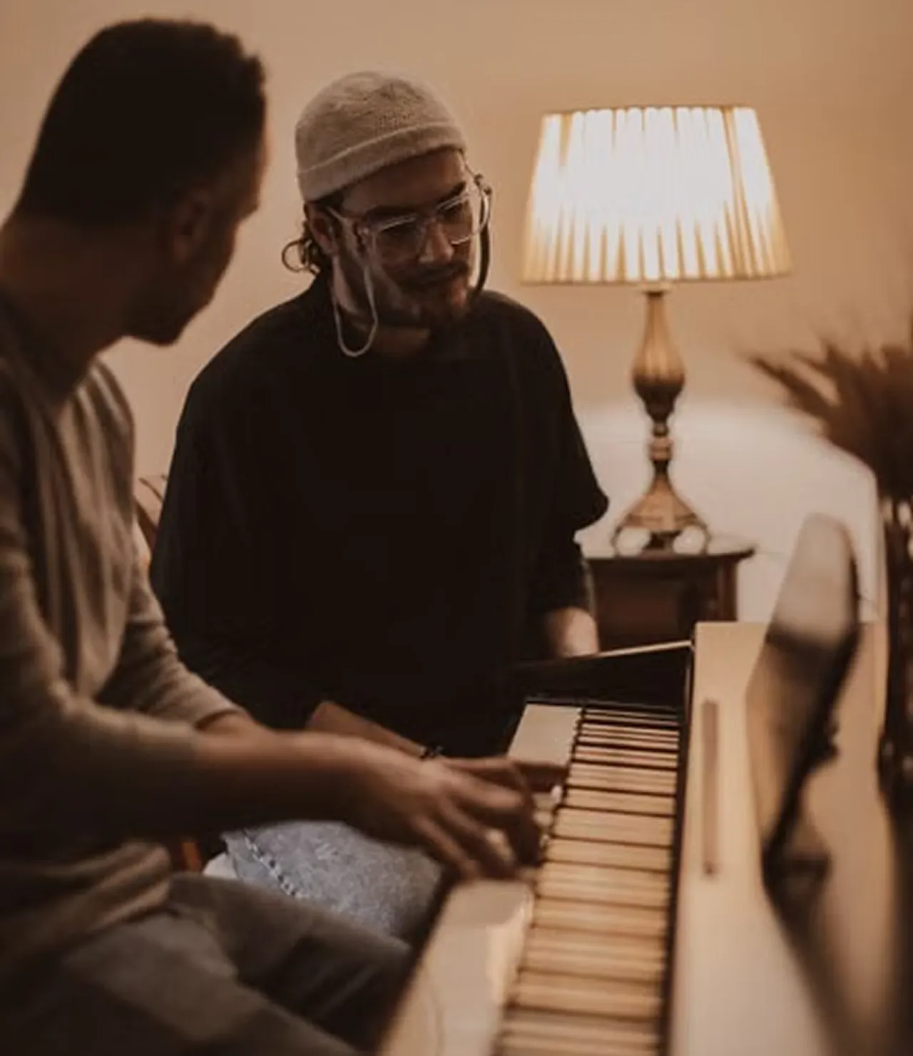 Two musicians writing a song together at a piano in a warmly lit room