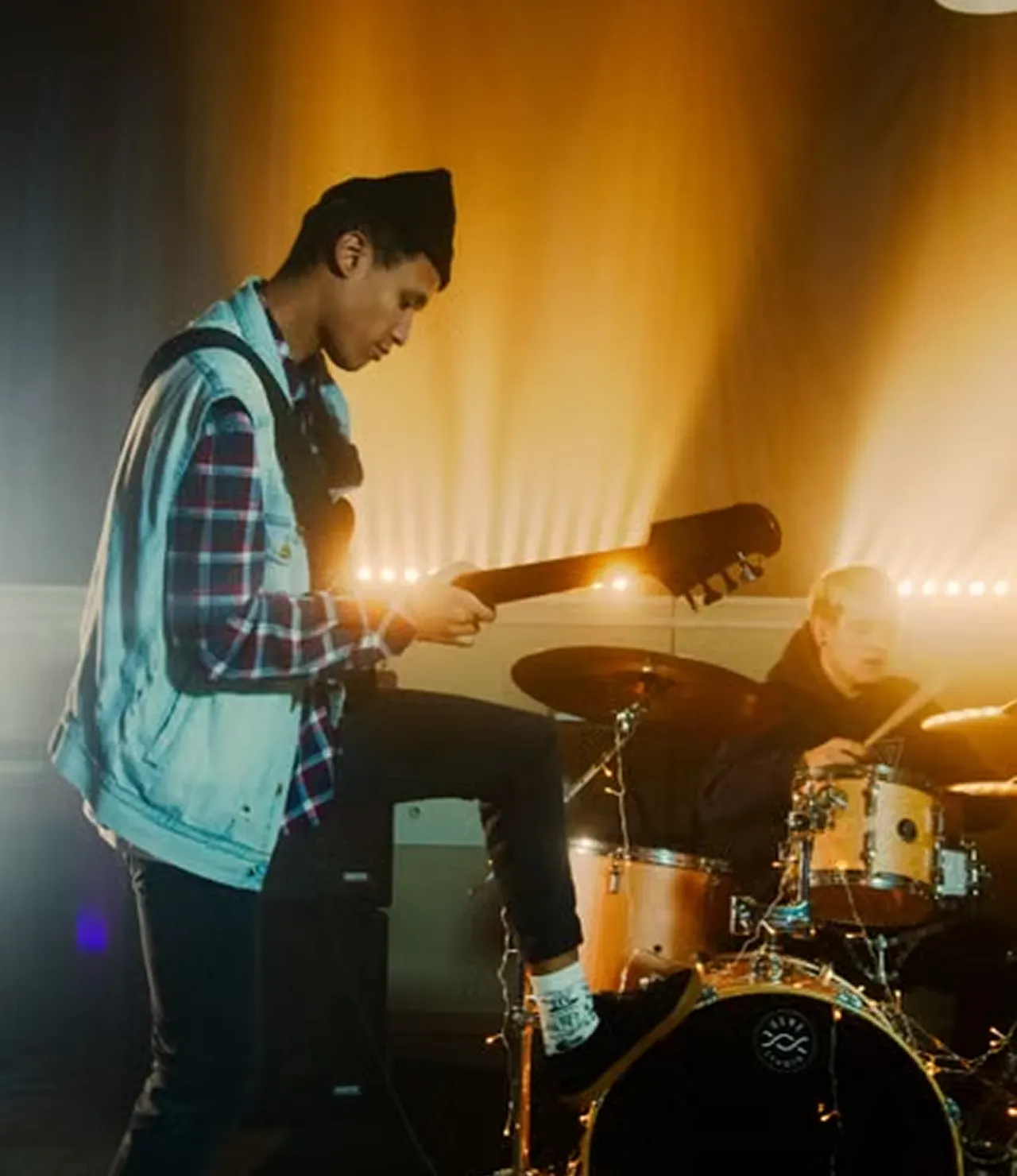 Guitarist and drummer performing live on stage under warm amber lights