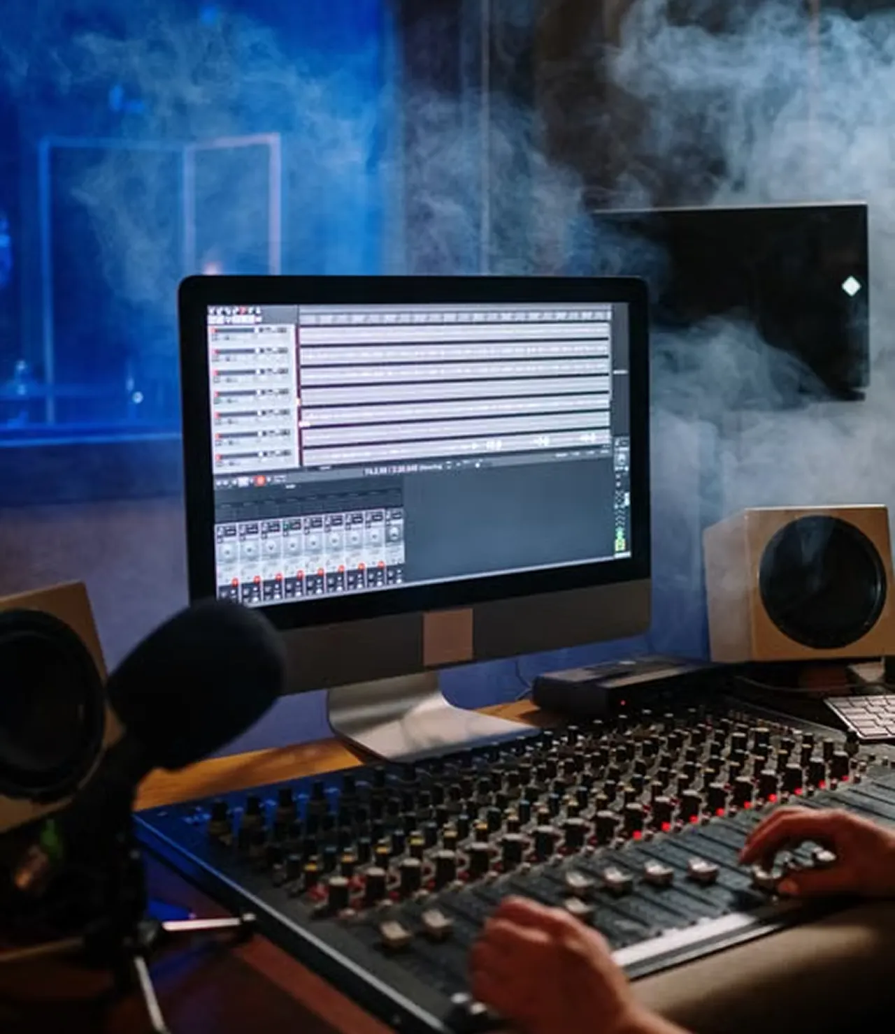 Producer adjusting faders on a mixing console beside a screen showing a recording session