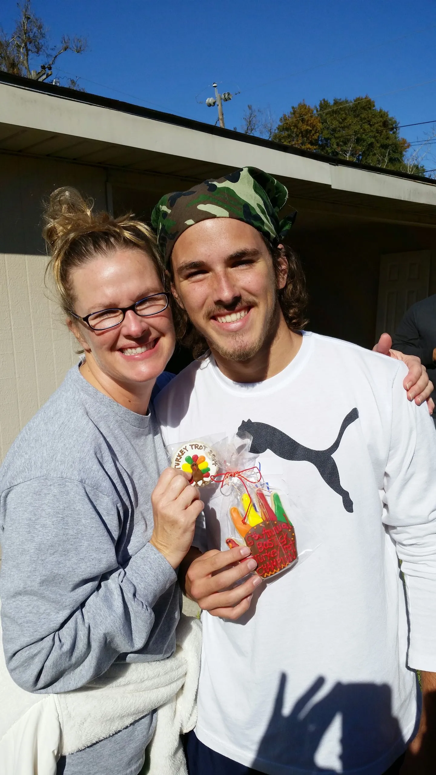 A smiling woman and a young man in a camo bandana posing outside a house