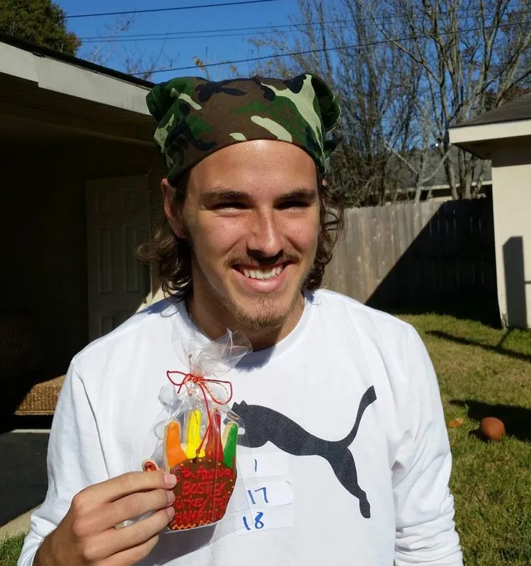 A young man in a camo bandana smiling and holding up a small prize