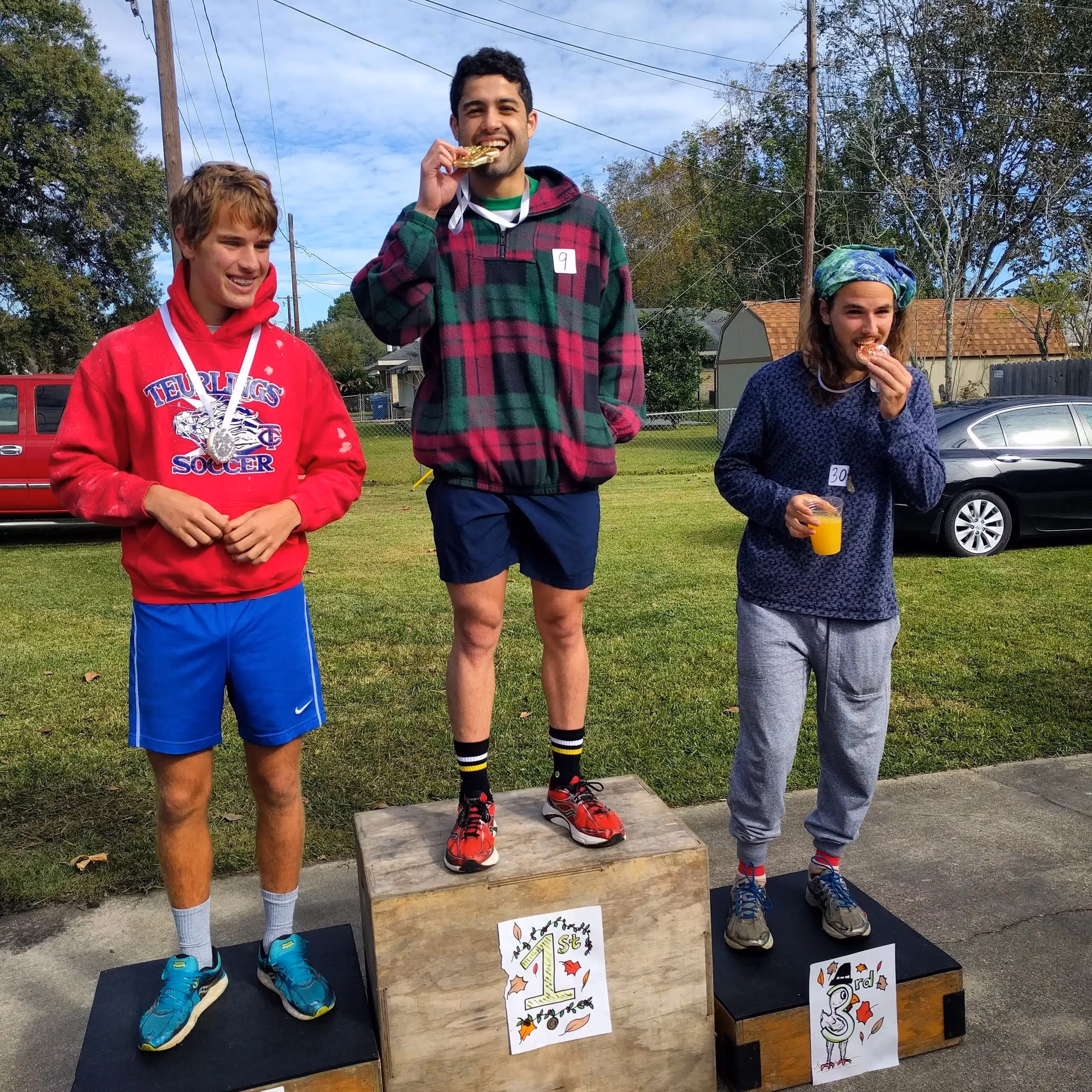 Three young runners on a homemade awards podium in a front yard