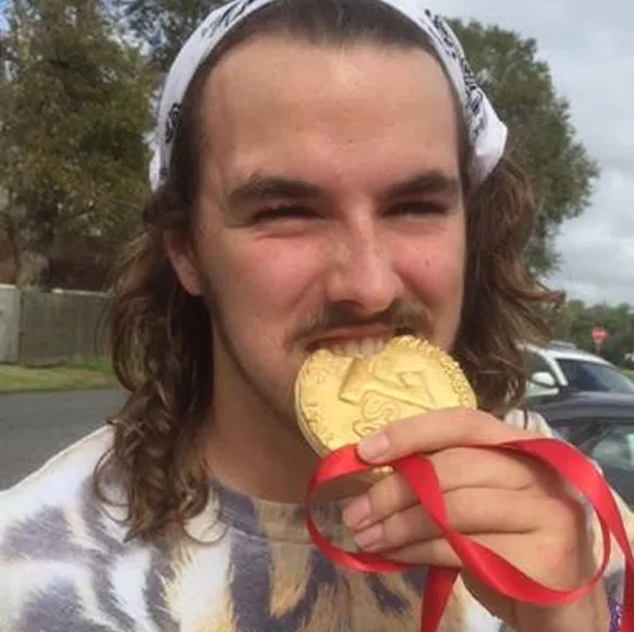 JeanPaul biting a gold medal with a big grin