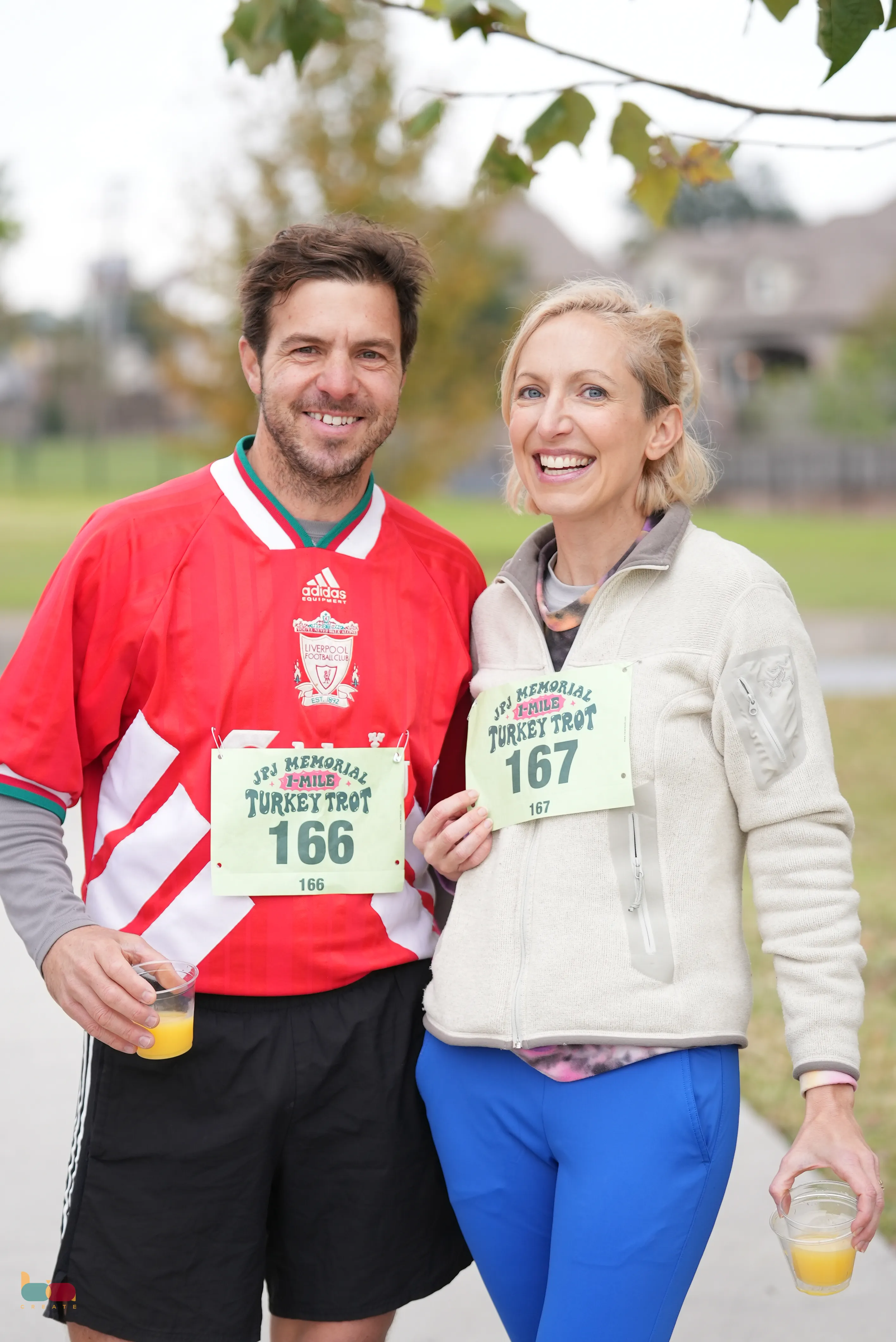 A smiling couple in race bibs holding drinks after the trot