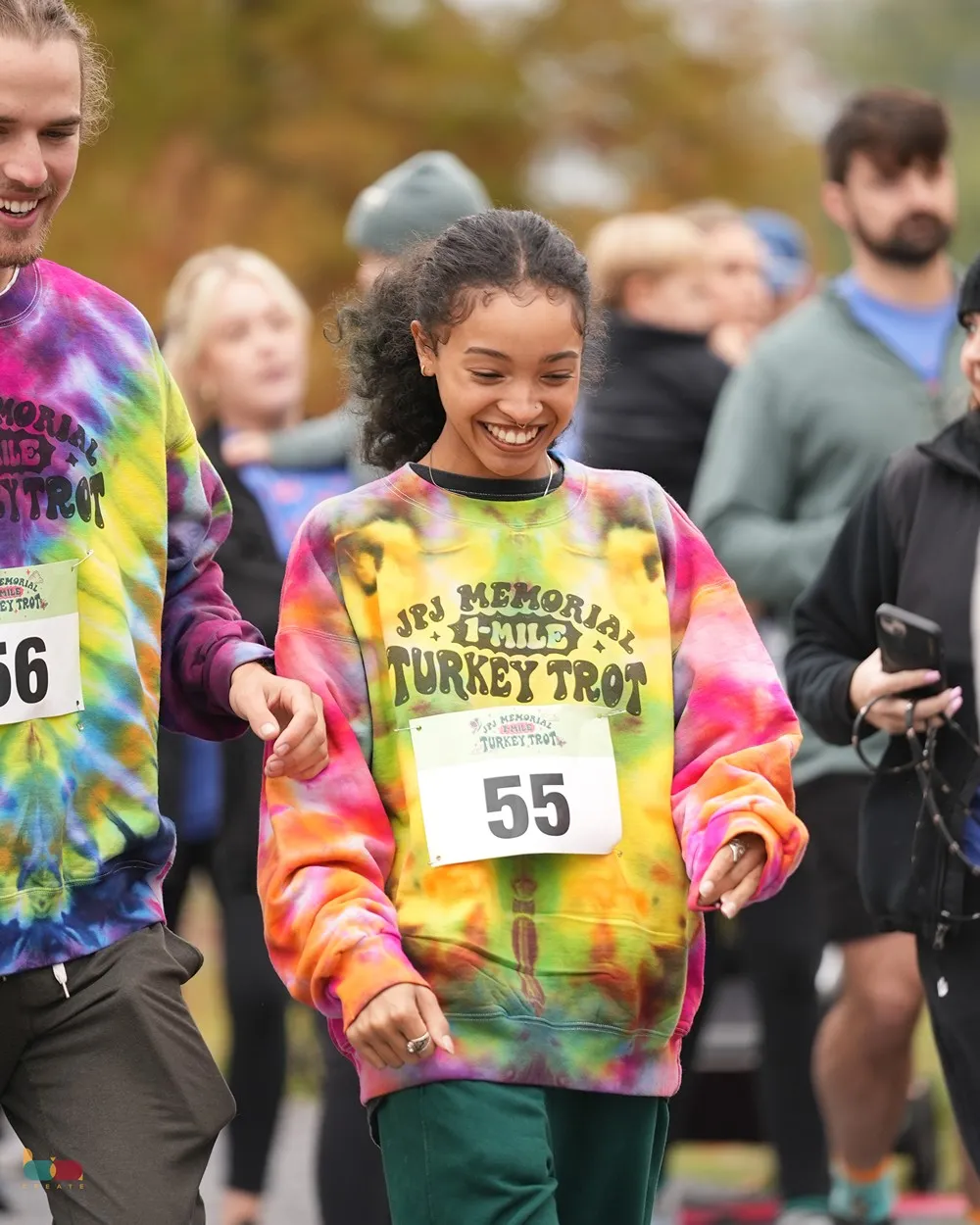 A runner in a tie-dye JPJ Memorial Turkey Trot shirt and race bib walking with the crowd