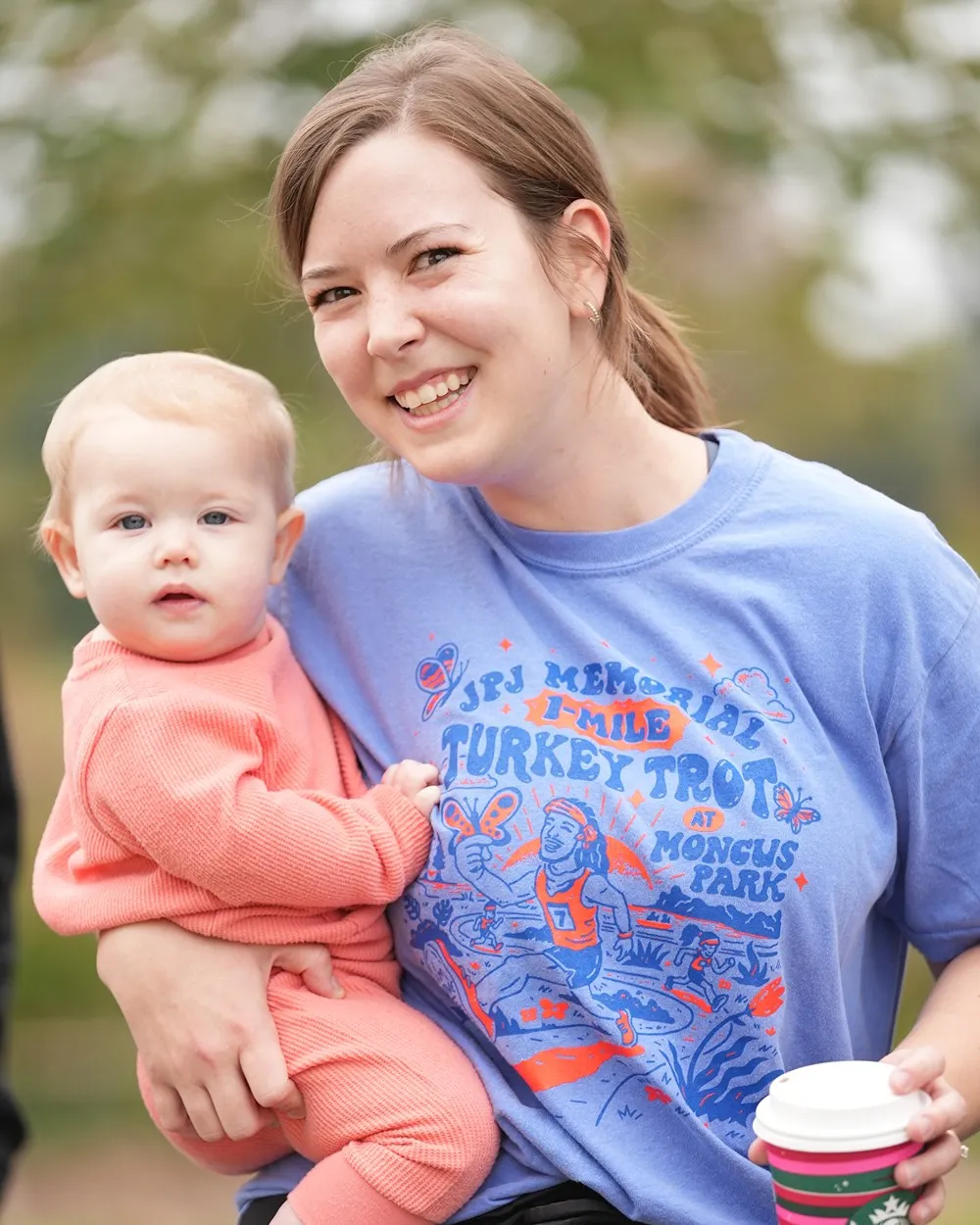 A smiling mom in a JPJ Turkey Trot shirt holding her baby