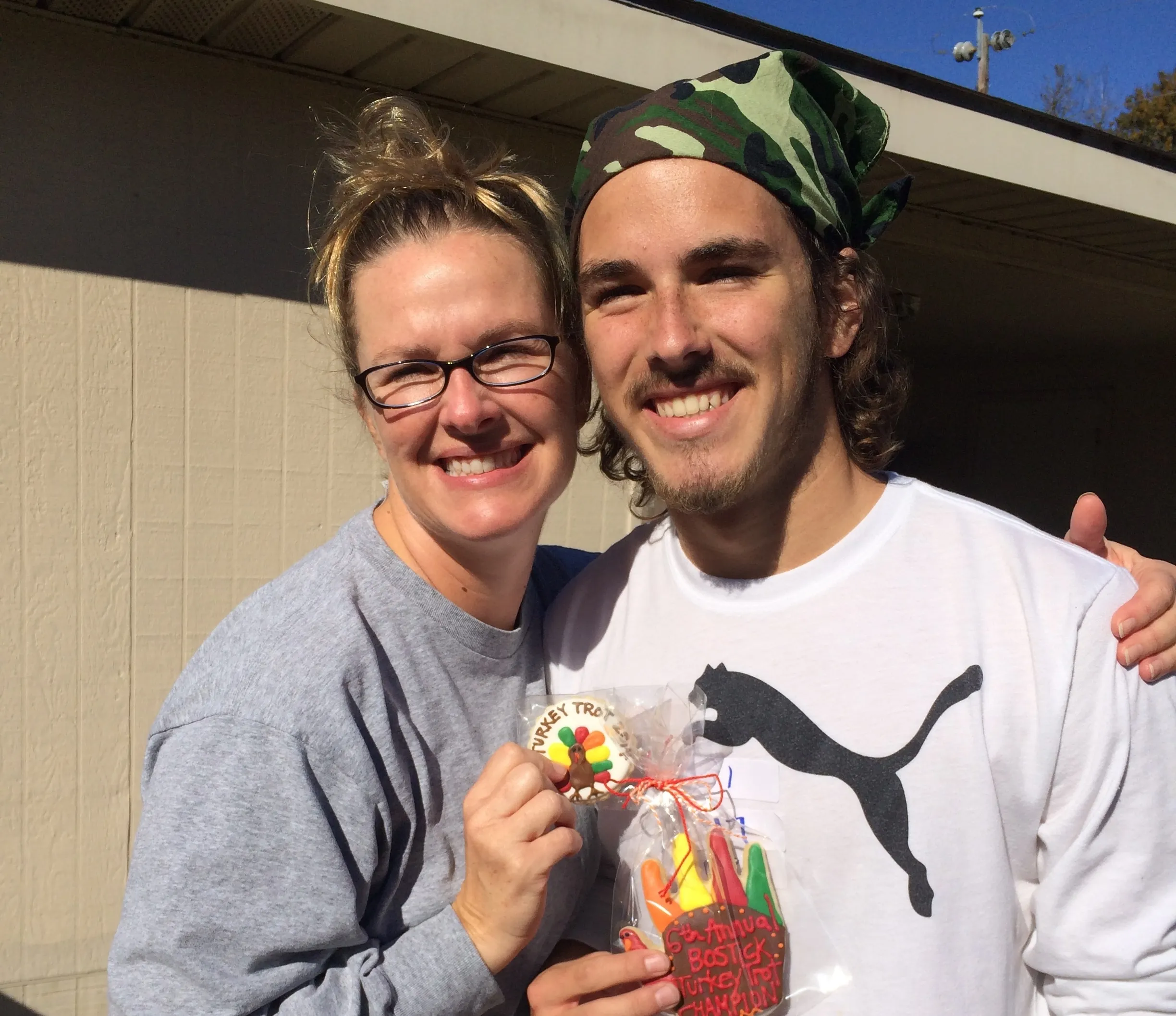 A smiling woman and a young man in a camo bandana holding up a wrapped turkey cookie prize
