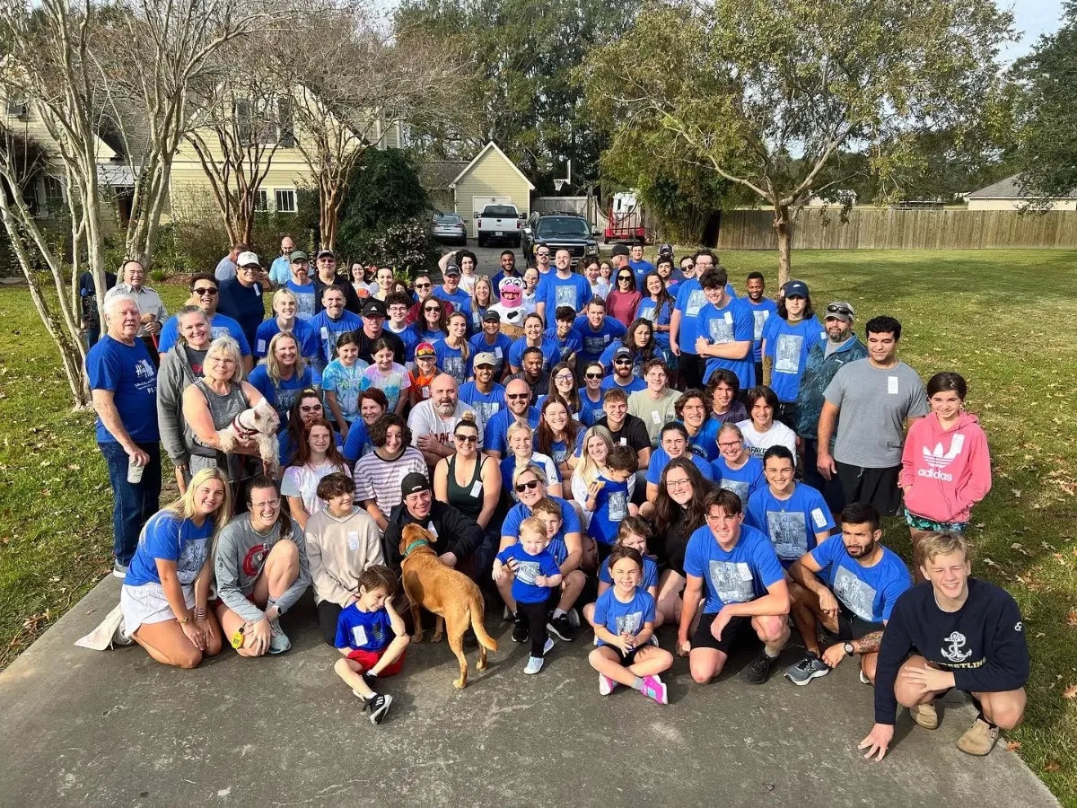 Dozens of runners in matching blue shirts posing for a group photo in a front yard