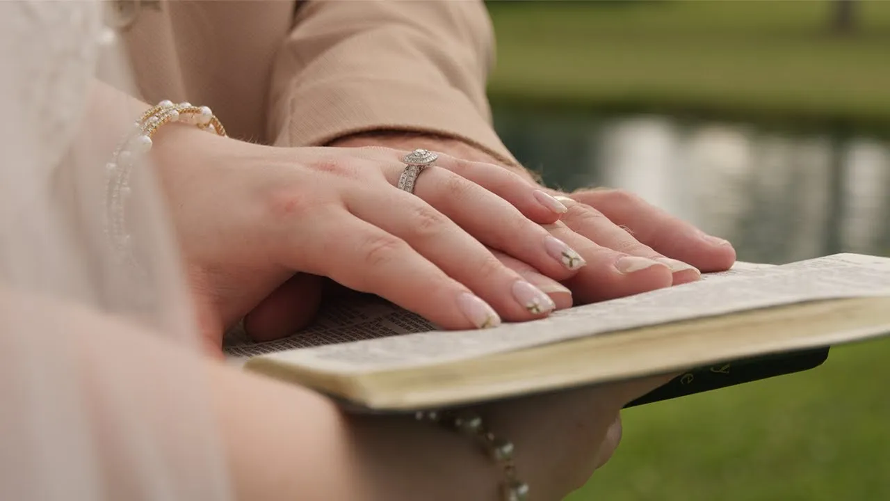 Holly and Brandon's hands resting on an open book on their wedding day, her ring catching the light
