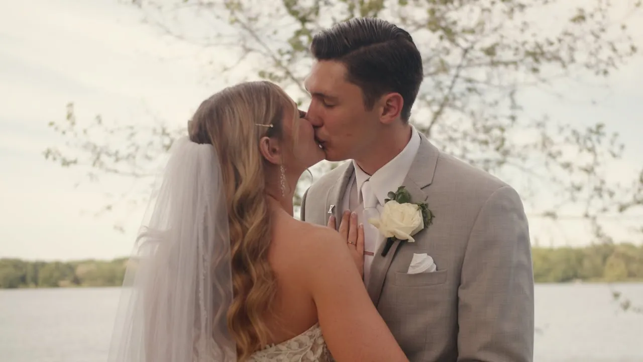Kelsey and Greg kissing at the edge of a lake on their wedding day
