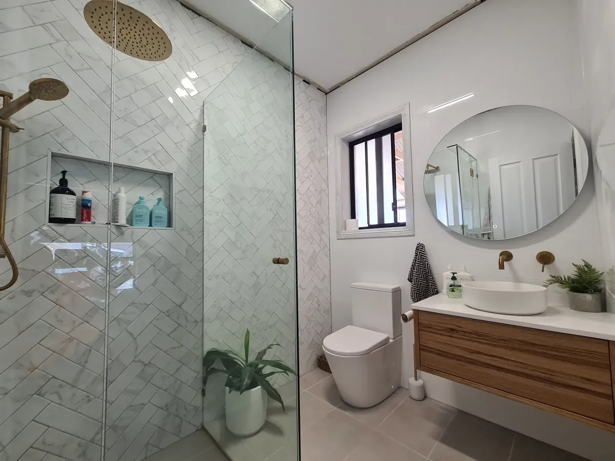 Shower with herringbone-pattern white wall tiles and a tiled niche beside a floating timber vanity