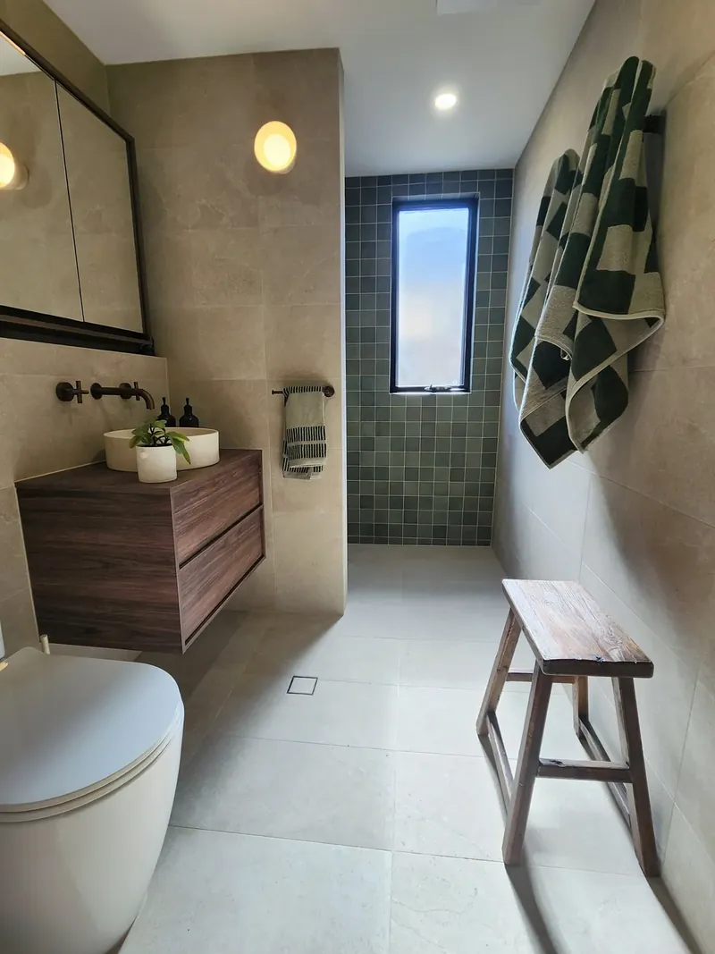 Bathroom with large-format beige wall and floor tiles, a green square-tile shower wall and a floating timber vanity