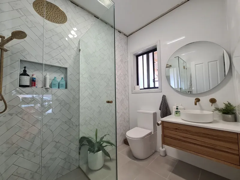 Shower with herringbone-pattern white wall tiles and a tiled niche beside a floating timber vanity