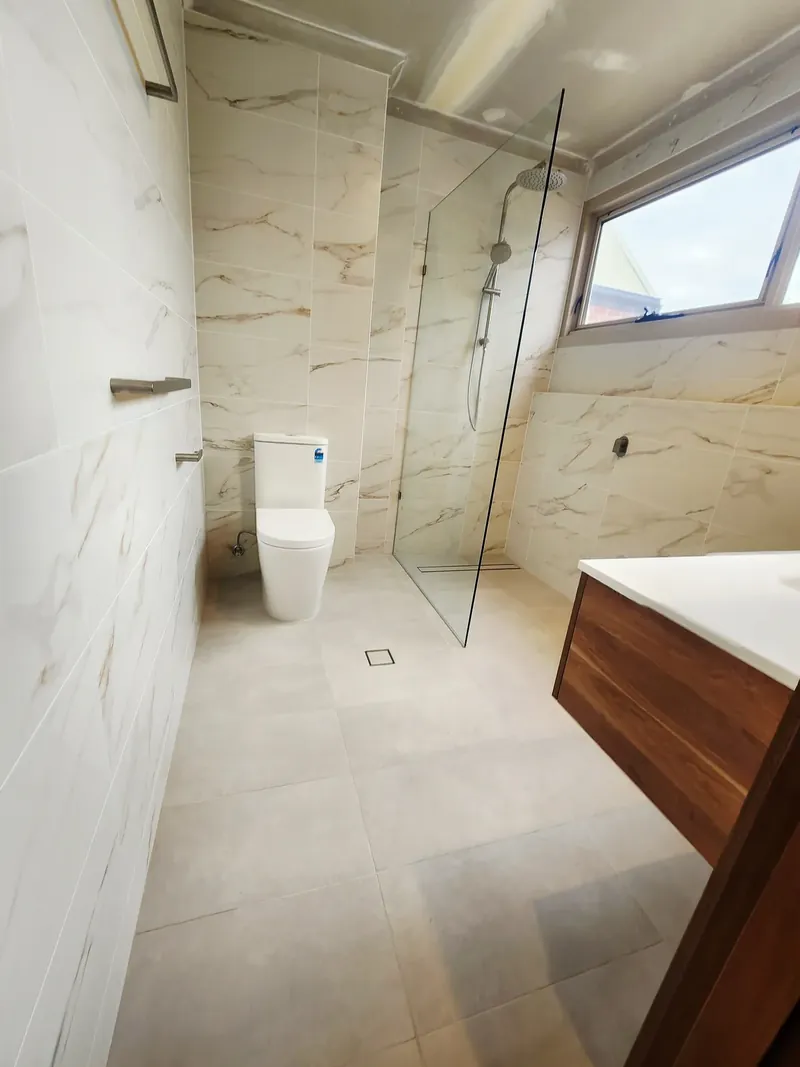 Bathroom with marble-look wall tiles with gold veining, light floor tiles and a glass shower panel