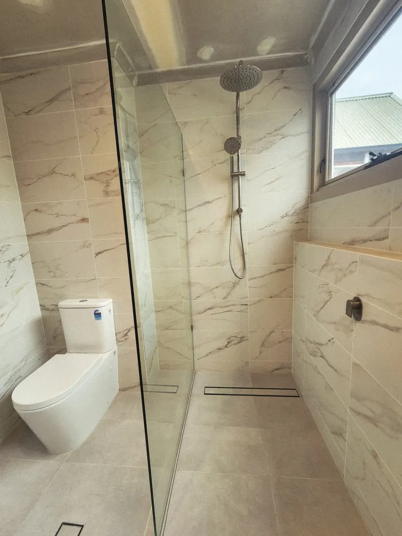 Shower with marble-look wall tiles with gold veining, light floor tiles and a linear floor drain