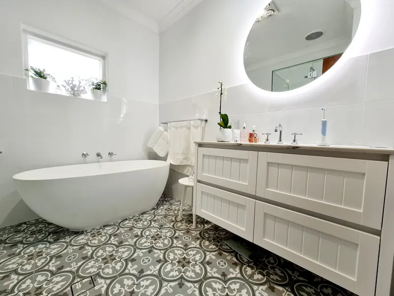 Bathroom with patterned floor tiles, a freestanding bath and a double vanity under a round mirror