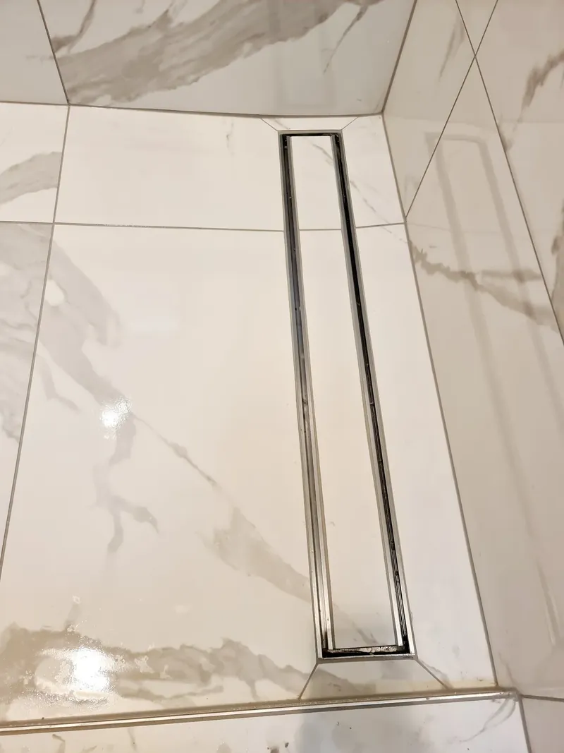 Large-format marble-look floor tiles with a stainless steel linear shower drain