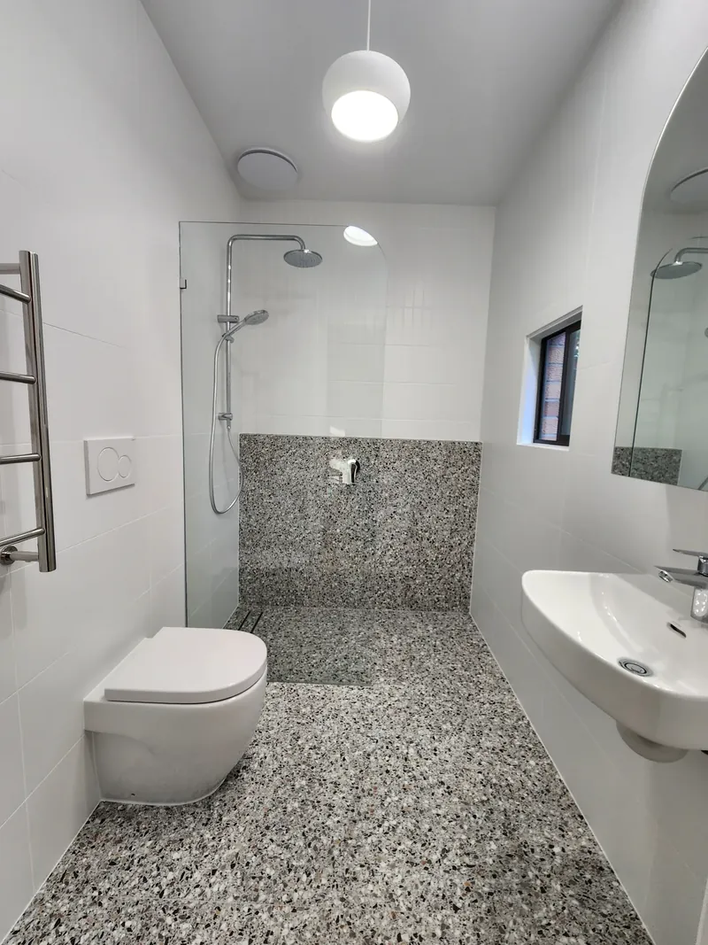 Bathroom with terrazzo-look floor tiles and wall dado, white wall tiles and a glass shower screen