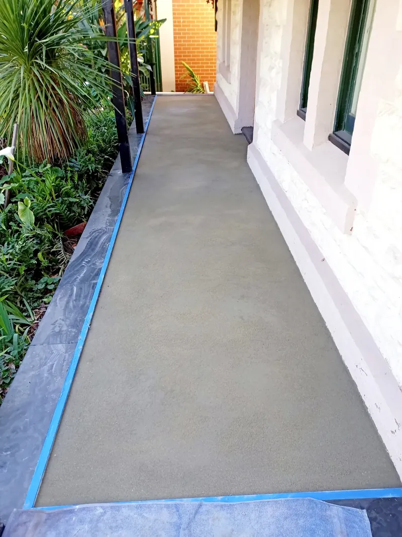 Level cement screed prepared for tiling along a side path, edged with blue tape