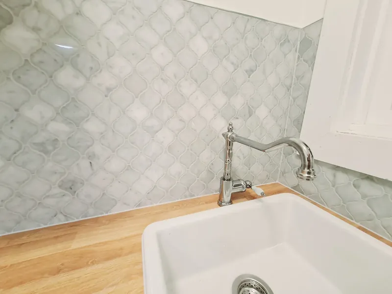 Marble-look arabesque-pattern splashback tiles behind a butler sink with a timber benchtop