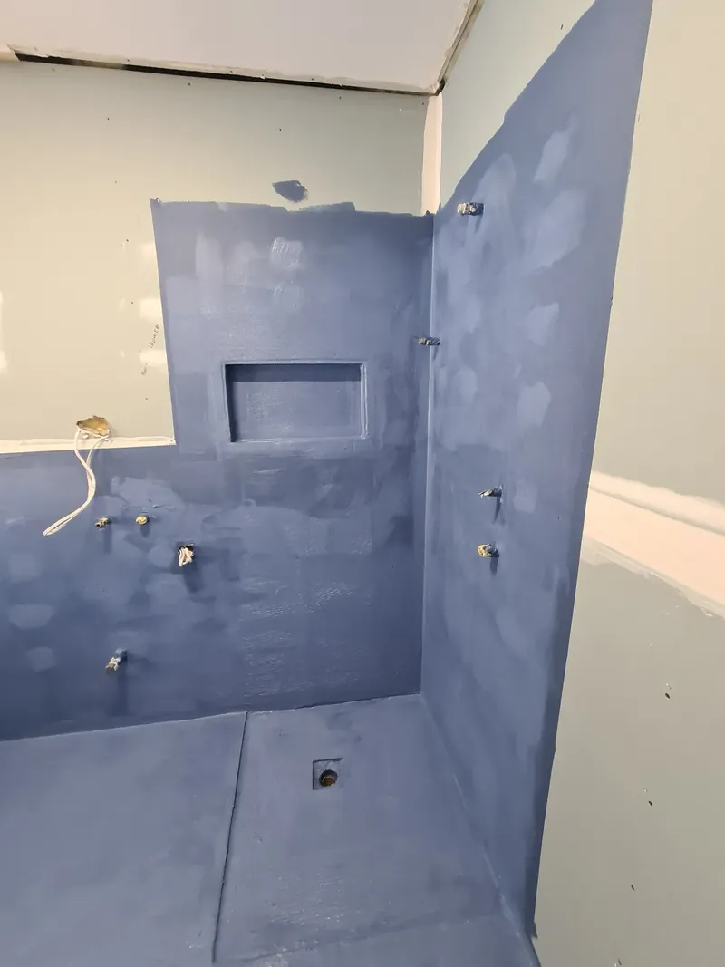 Shower recess with blue waterproofing membrane on the walls and floor, a recessed niche and a floor waste, before tiling