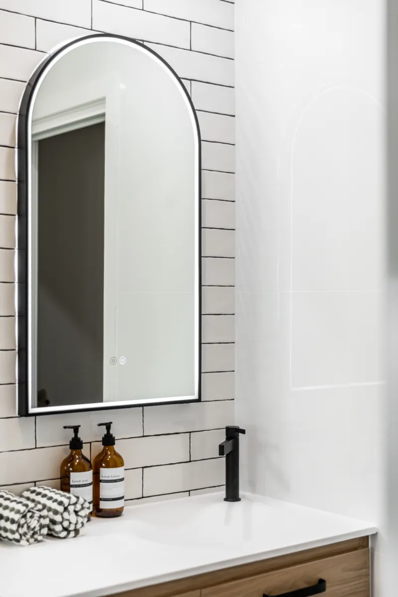Ensuite in Norwood with white subway wall tiles, an arched black-framed mirror and a timber vanity