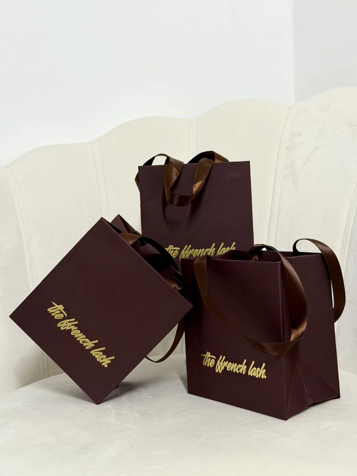 Burgundy The Ffrench Lash gift bags with satin ribbon handles on a cream velvet chair