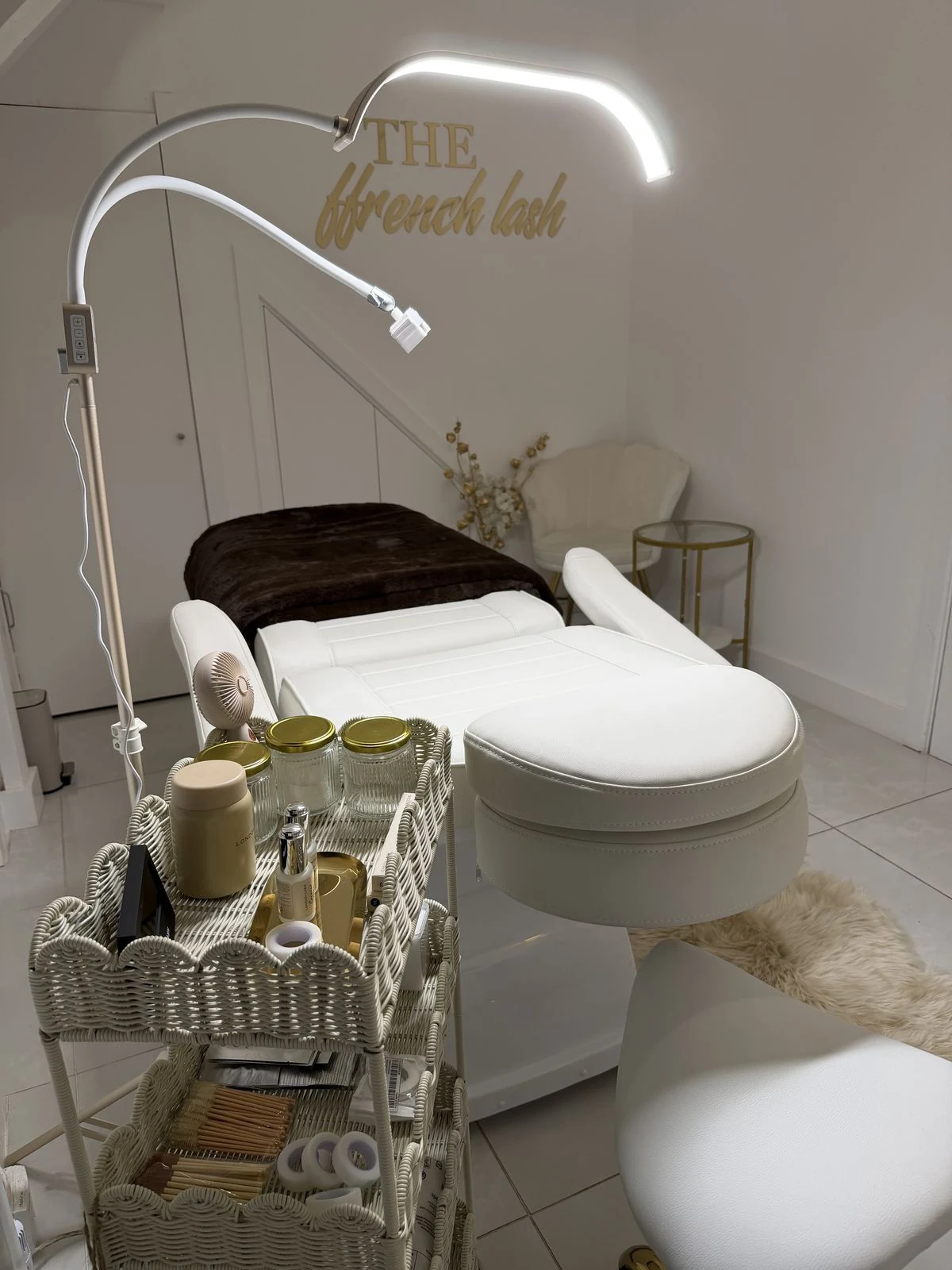 A wicker lash trolley, lash lamp and treatment bed under the gold Ffrench Lash sign