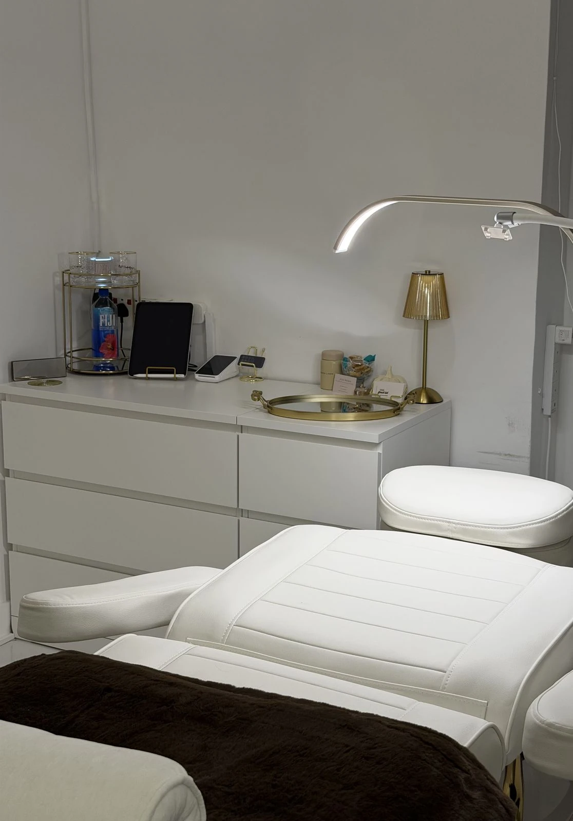 A white lash bed and curved lash lamp beside a gold vanity lamp in the studio