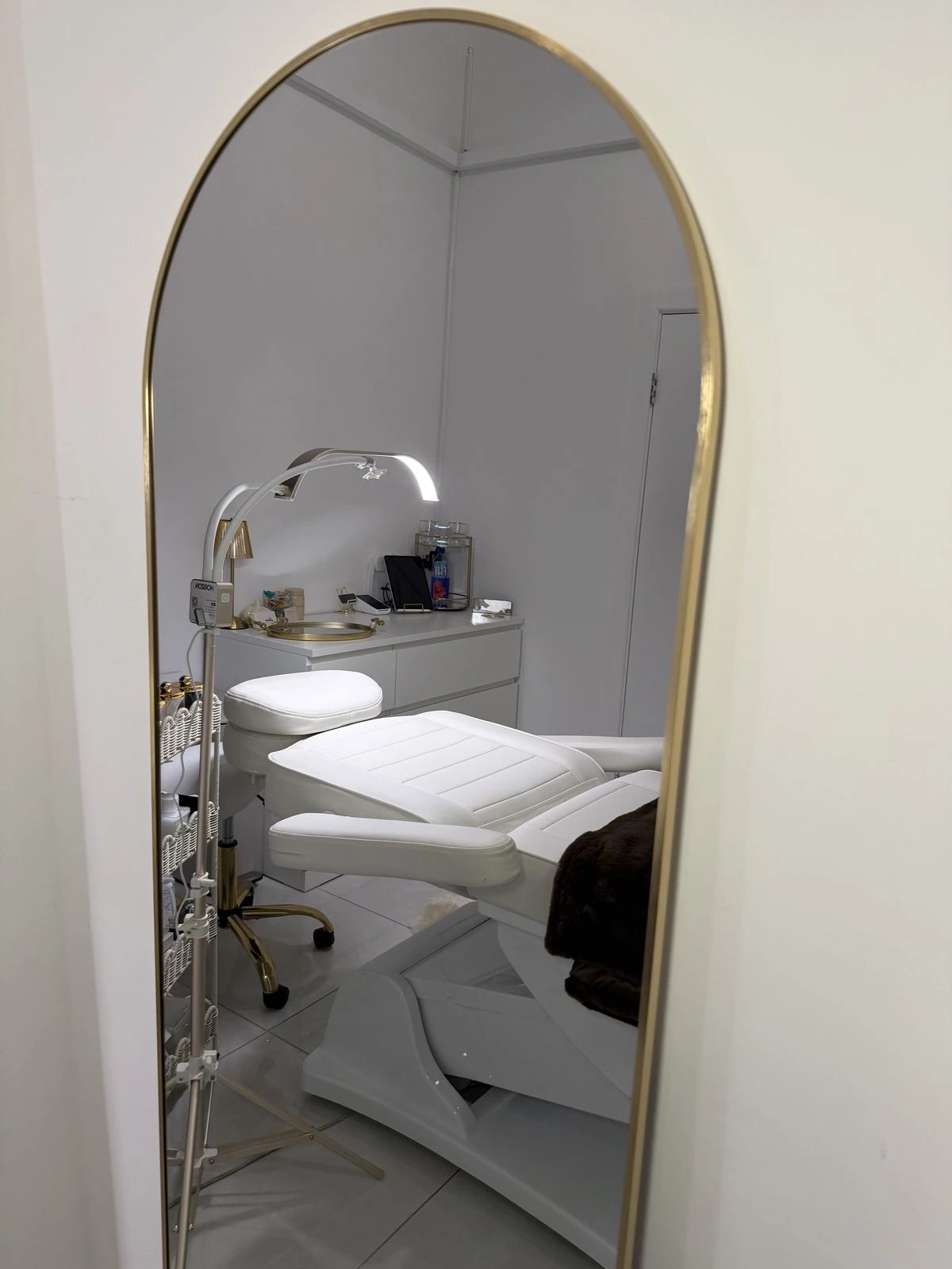 The treatment room reflected in a tall arched gold mirror