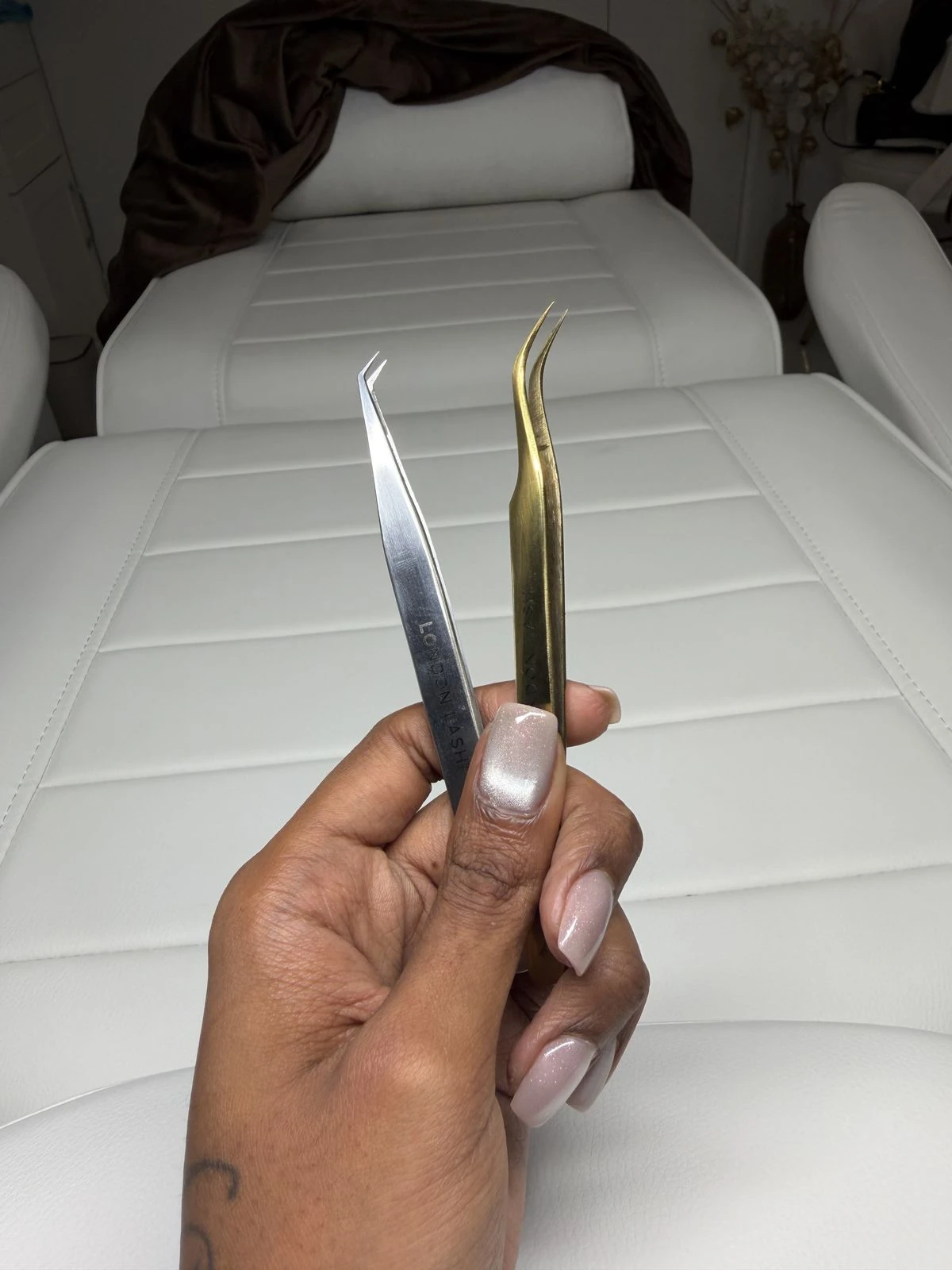 Jordy holding her silver and gold lash tweezers over the treatment bed