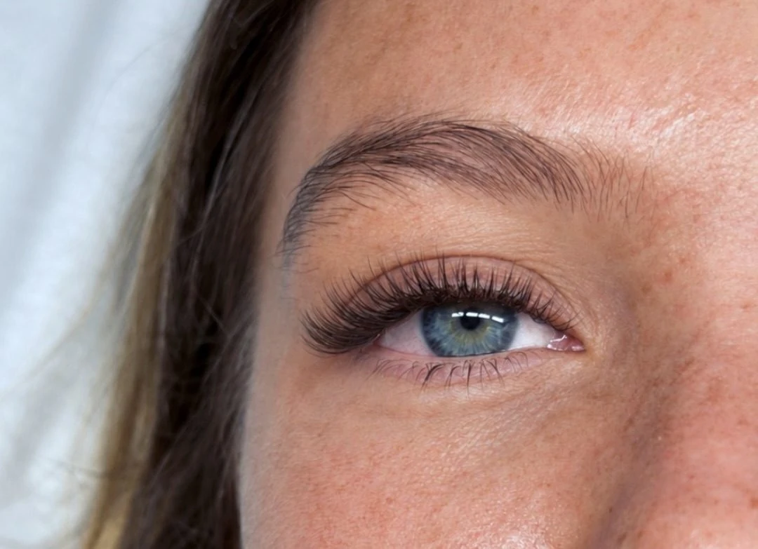 Close-up of a soft, natural lash extension set on a blue eye