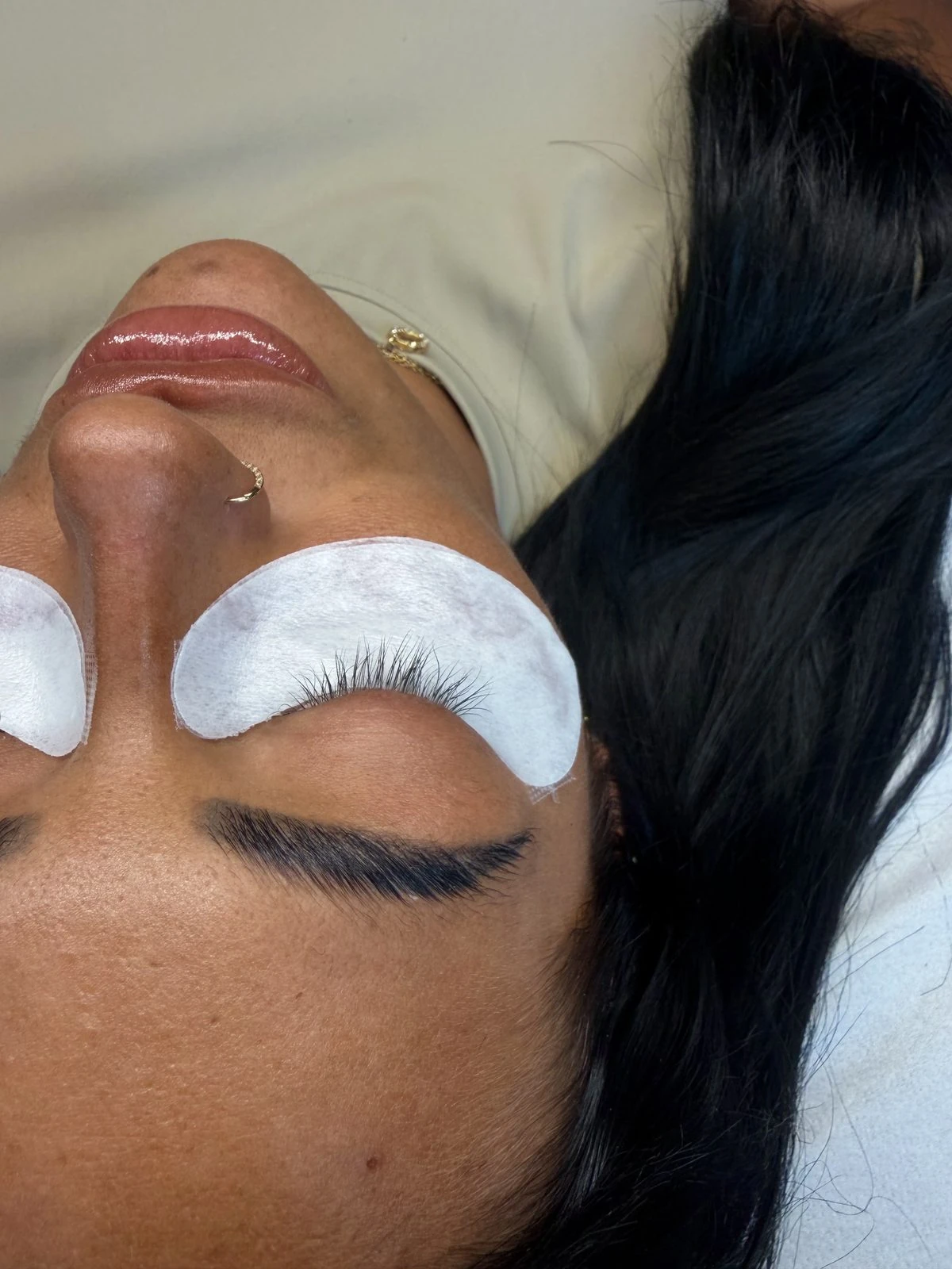 A client resting with eyes closed under white eye pads, showing a fresh set of lash extensions
