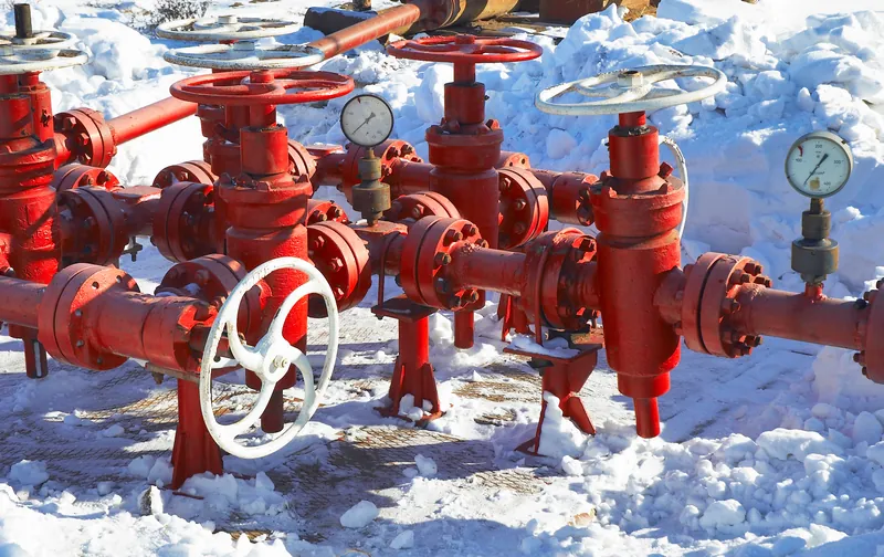 Red valves and gauges on piping surrounded by snow