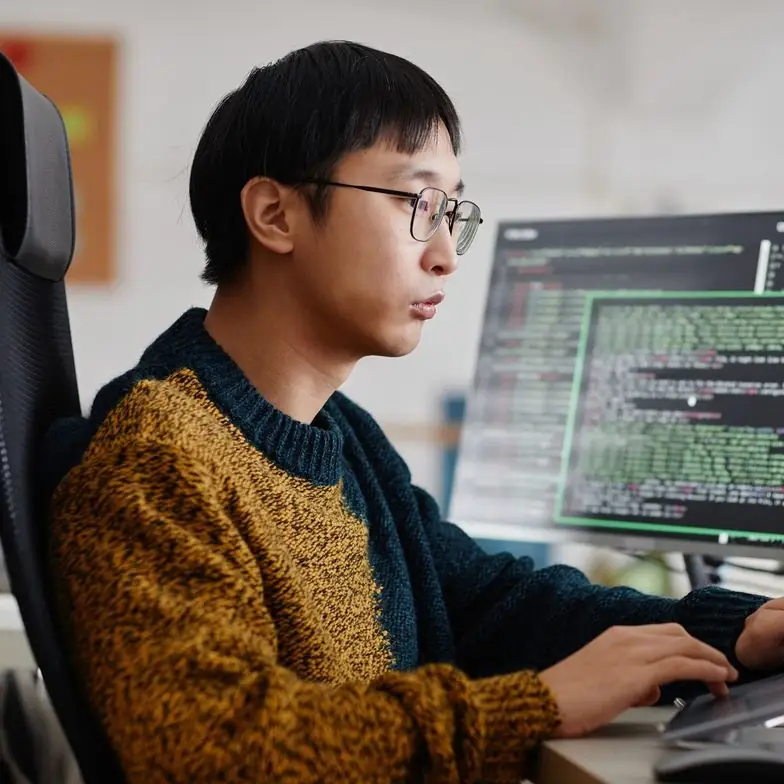 Developer in a knit sweater coding at his monitors