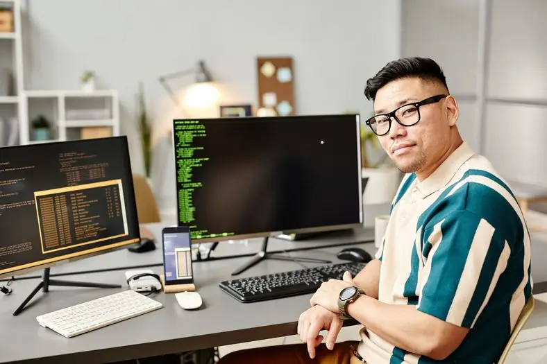 IT lead in a striped shirt at his desk with code on his monitors